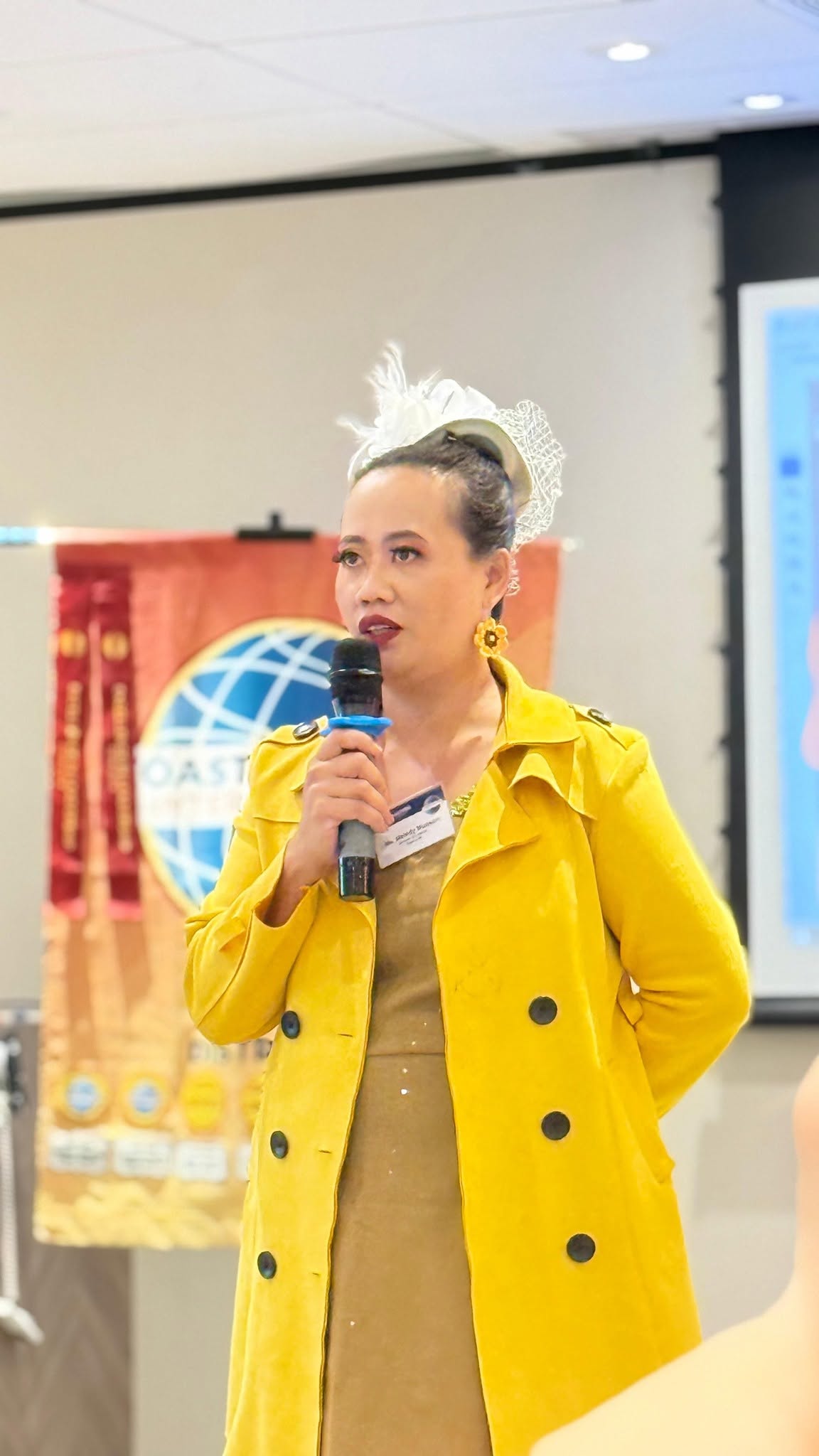 Melody Munson in a yellow coat, speaking into a microphone